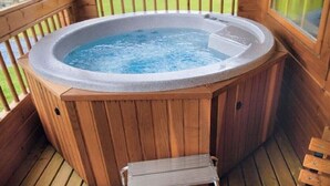 Una bañera de madera caliente en una terraza con una escalera de metal y un banco de madera.