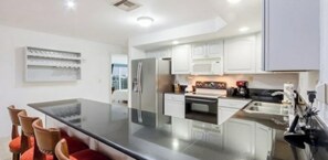A modern kitchen with white cabinetry, a stainless steel refrigerator, and a black countertop.
