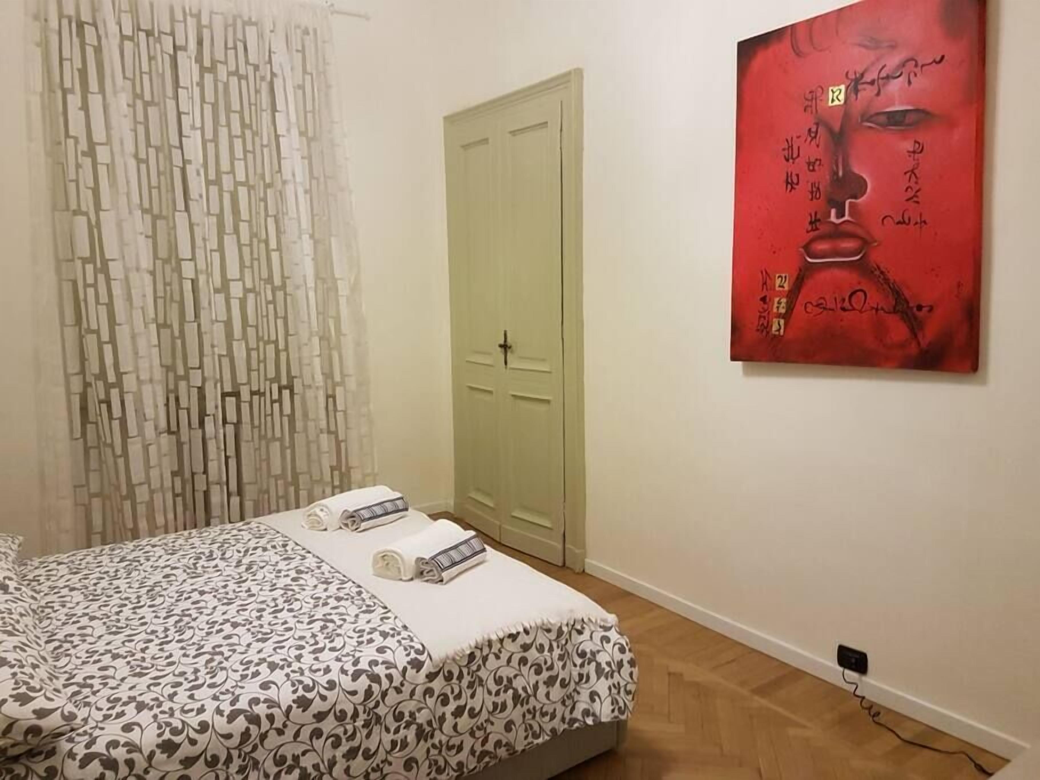 A bedroom with a bed, a green door, and a red artwork on the wall.
