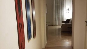 A hallway with a wooden floor leading to a room with a white curtain and a lamp.