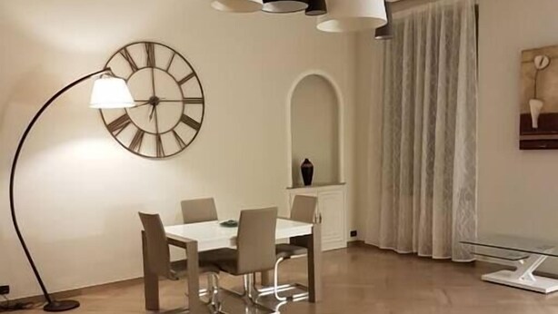 A modern dining area with a round table and chairs, a floor lamp, and a wall clock.