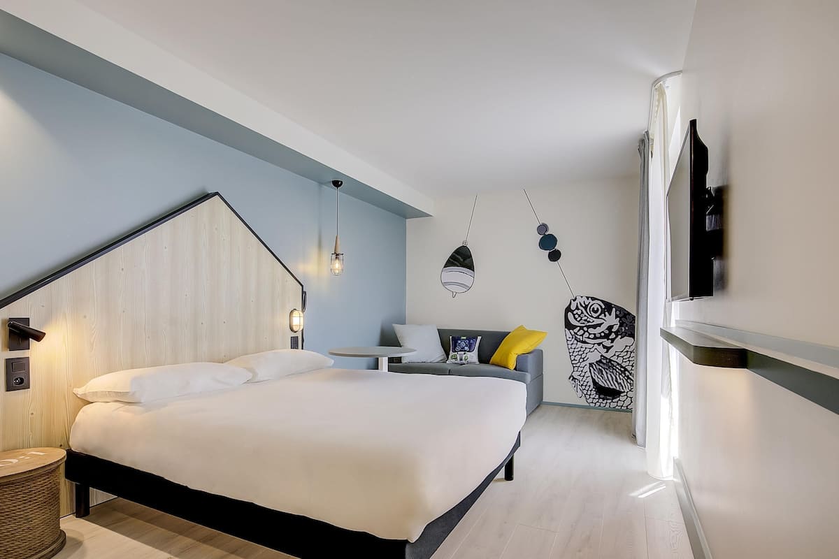 Une chambre d’hôtel moderne équipée d’un lit, d’une table de chevet, d’une lampe et d’un téléviseur fixé au mur.