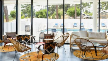 Un área de descanso moderna con mobiliario de mimbre, vista a la piscina y ventanas amplias.