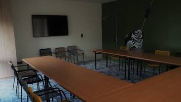 A conference room with a long table, several chairs, a flat-screen TV on the wall, and a patterned carpet.