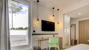 Een moderne hotelkamer met een groot bed, een bureau met stoel, een aan de muur bevestigde televisie en een raam met uitzicht op bomen.