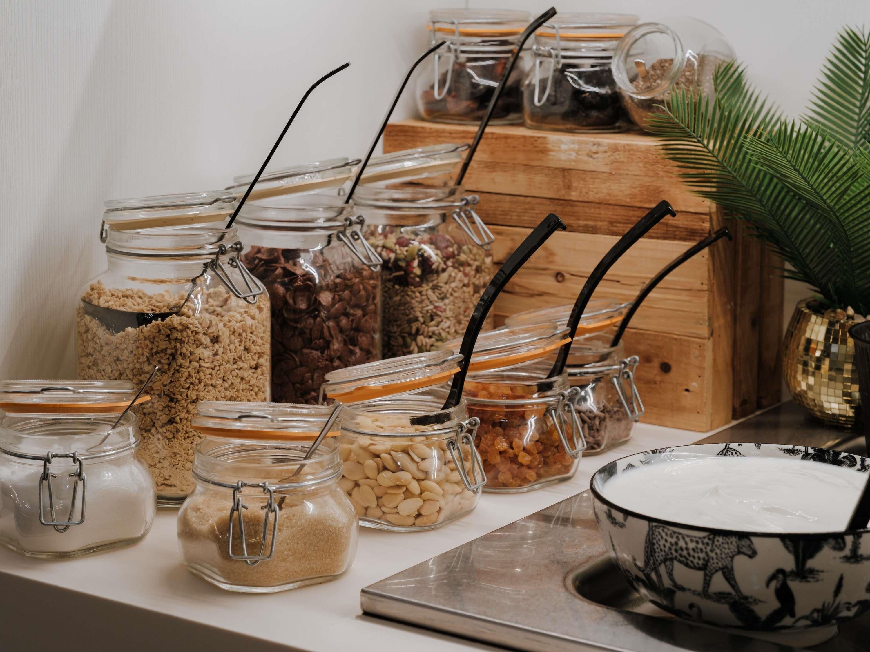 A variety of food items in glass jars with metal clasps, some with black straws inserted, on a wooden surface.