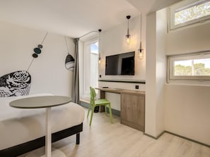 Une cuisine moderne avec un coin repas, un téléviseur à écran plat fixé au-dessus d’un comptoir en bois, et une fenêtre laissant entrer la lumière naturelle.
