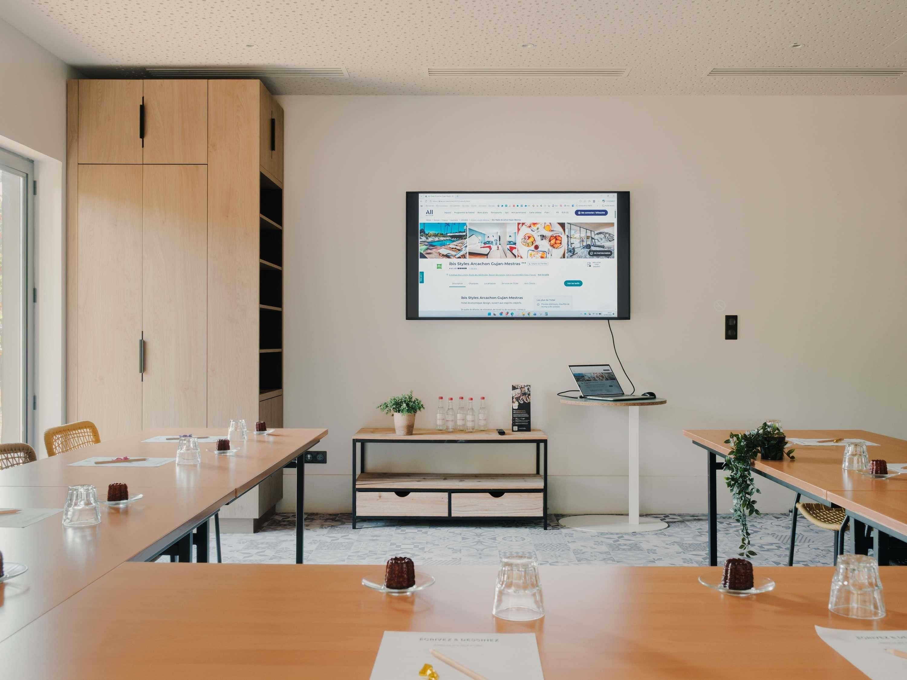A conference room with a large screen displaying a webpage, wooden furniture, and a small table with a laptop.