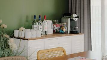Quarto de hotel com mesa de jantar, armários brancos, máquina de café e objetos decorativos.