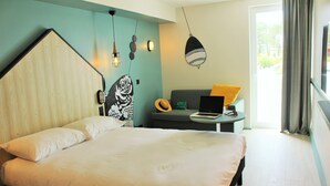 Une chambre moderne avec un grand lit, un bureau avec un ordinateur portable et une vue sur l’extérieur.