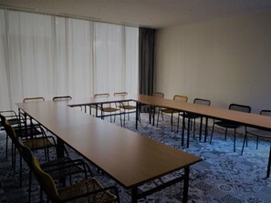 Een vergaderruimte met een lange tafel en stoelen, grote ramen voorzien van gordijnen en een kamerbreed tapijt met een patroon.