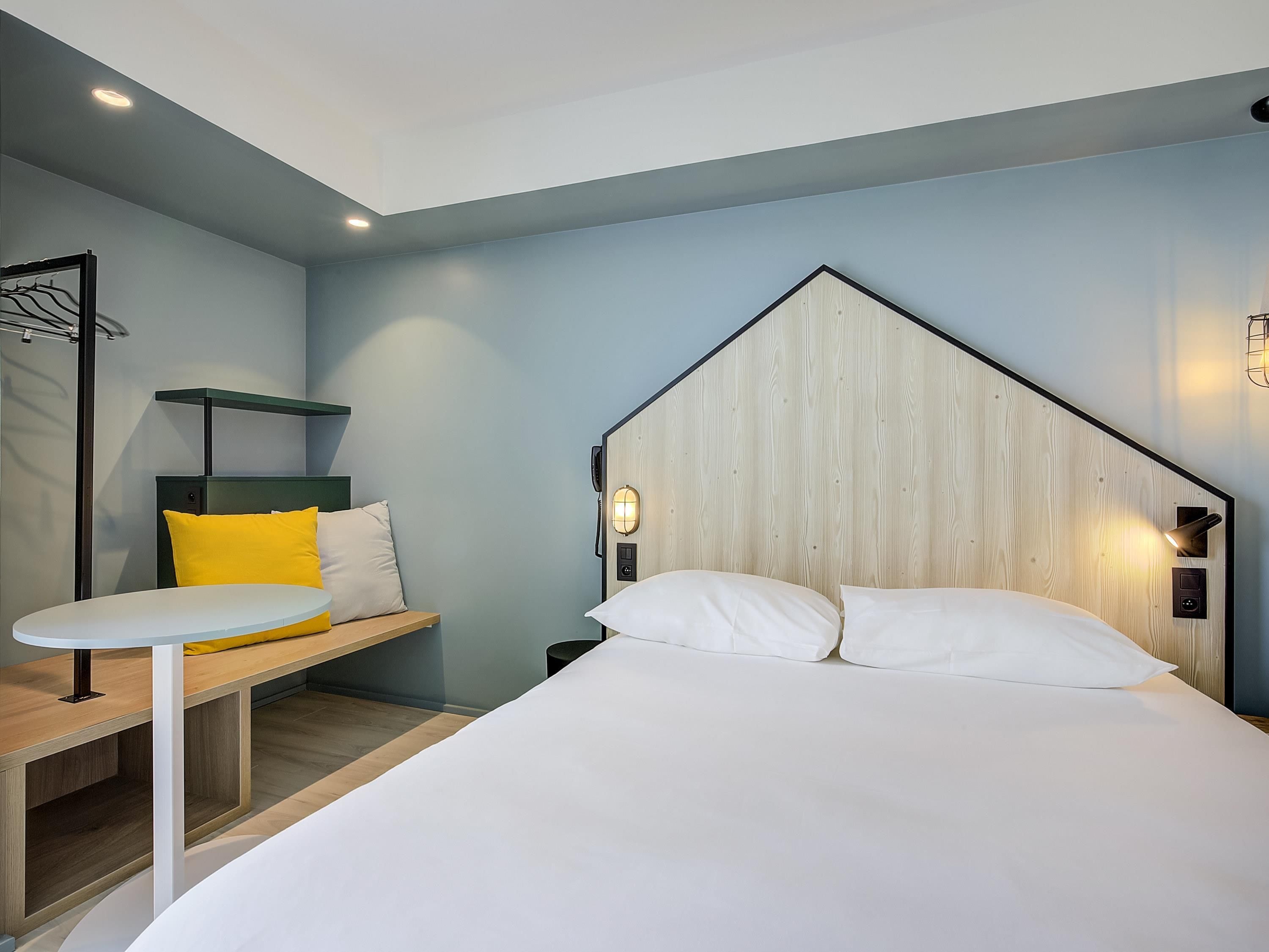 A modern hotel room with a bed, bedside table, and a bench with cushions.