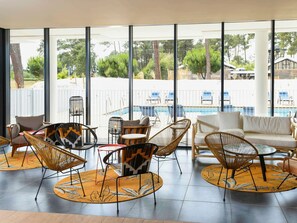 A modern lounge area with wicker furniture, a pool view, and large windows.