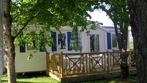 A row of mobile homes with a wooden deck and a tree in the foreground. - Camping Les Tilleuls - Mobilhome (Rocamadour)
