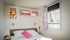 A neatly arranged bedroom with a bed, bedside tables, and built-in shelves with pillows and books. - Camping Les Tilleuls - Mobilhome (Rocamadour)