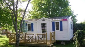 A small, single-story mobile home with a front deck and a covered patio area. - Camping Les Tilleuls - Mobilhome (Rocamadour)
