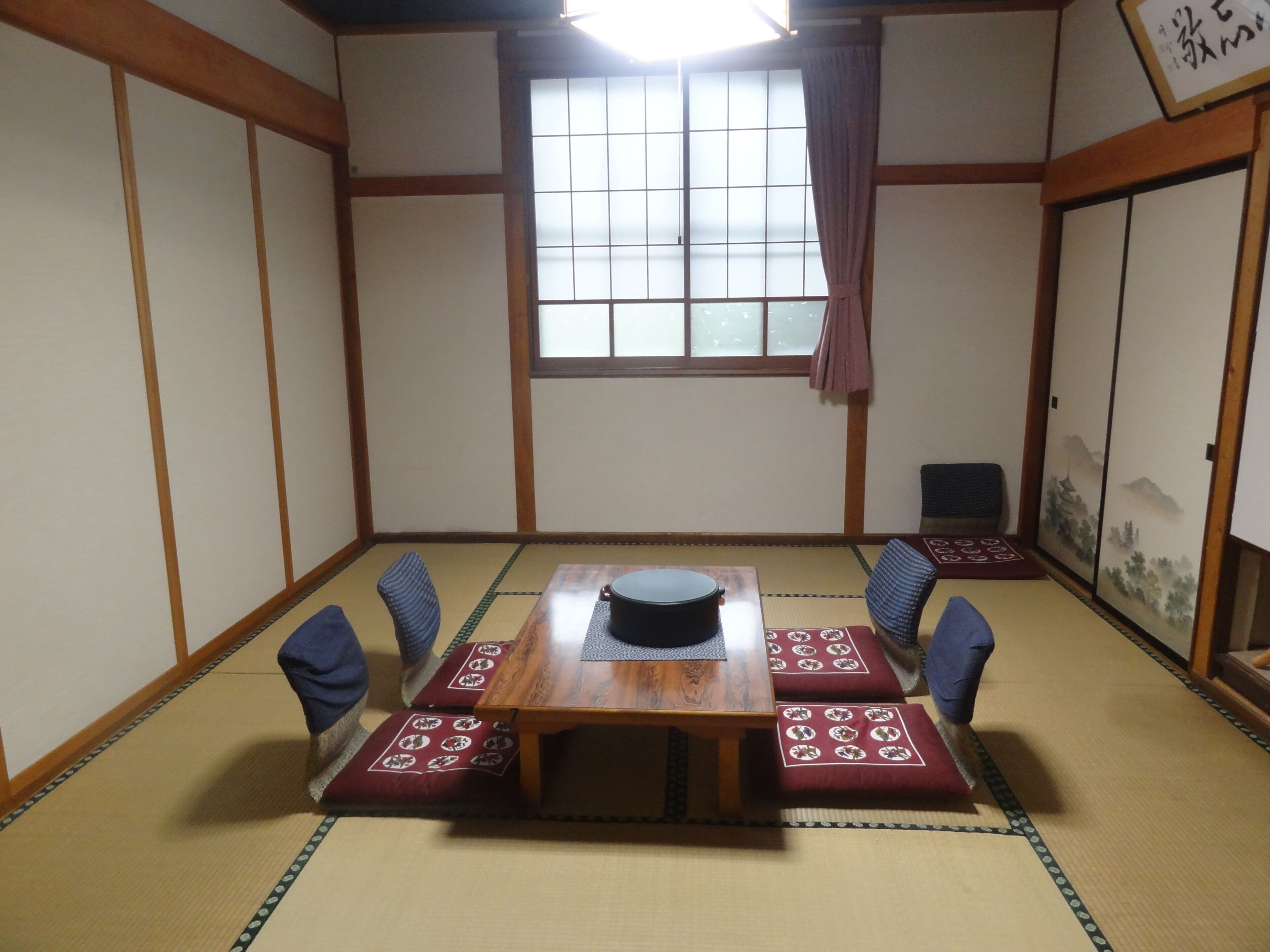 A traditional Japanese room with tatami flooring, a wooden table with a black object on it, and a shoji screen with a landscape painting.