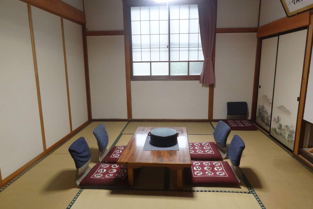 Um quarto tradicional japonês com tatames, uma mesa de madeira com um objeto preto sobre ela e um painel shoji com uma pintura de paisagem.