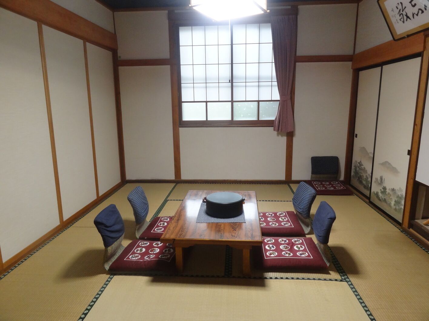 A traditional Japanese room with tatami flooring, a wooden table with a black pot, and a shoji screen with a landscape painting.