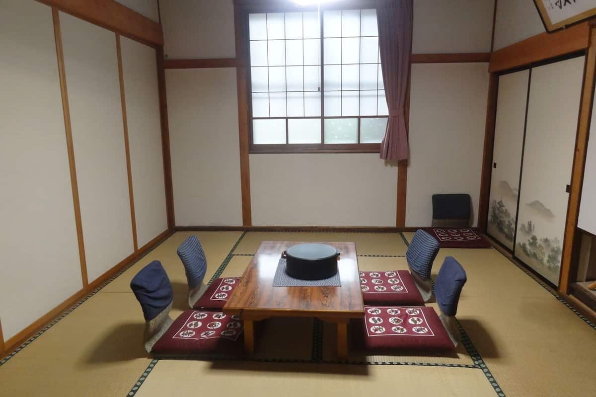 Um quarto japonês tradicional com tatames, uma mesa de madeira com uma panela preta e um shoji com pintura de paisagem.