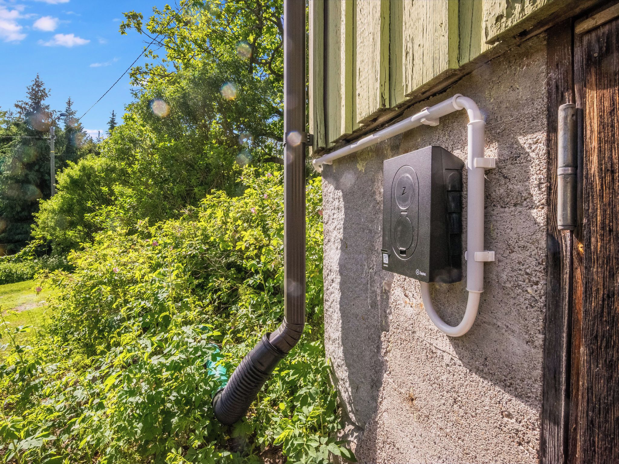 A building with a weathered exterior, a visible gutter system, and a small electrical box mounted on the wall.
