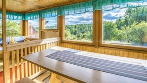 A wooden cabin with a large dining table, two windows with curtains, and a view of a forest. - Palttala by Interhome (Tampere)