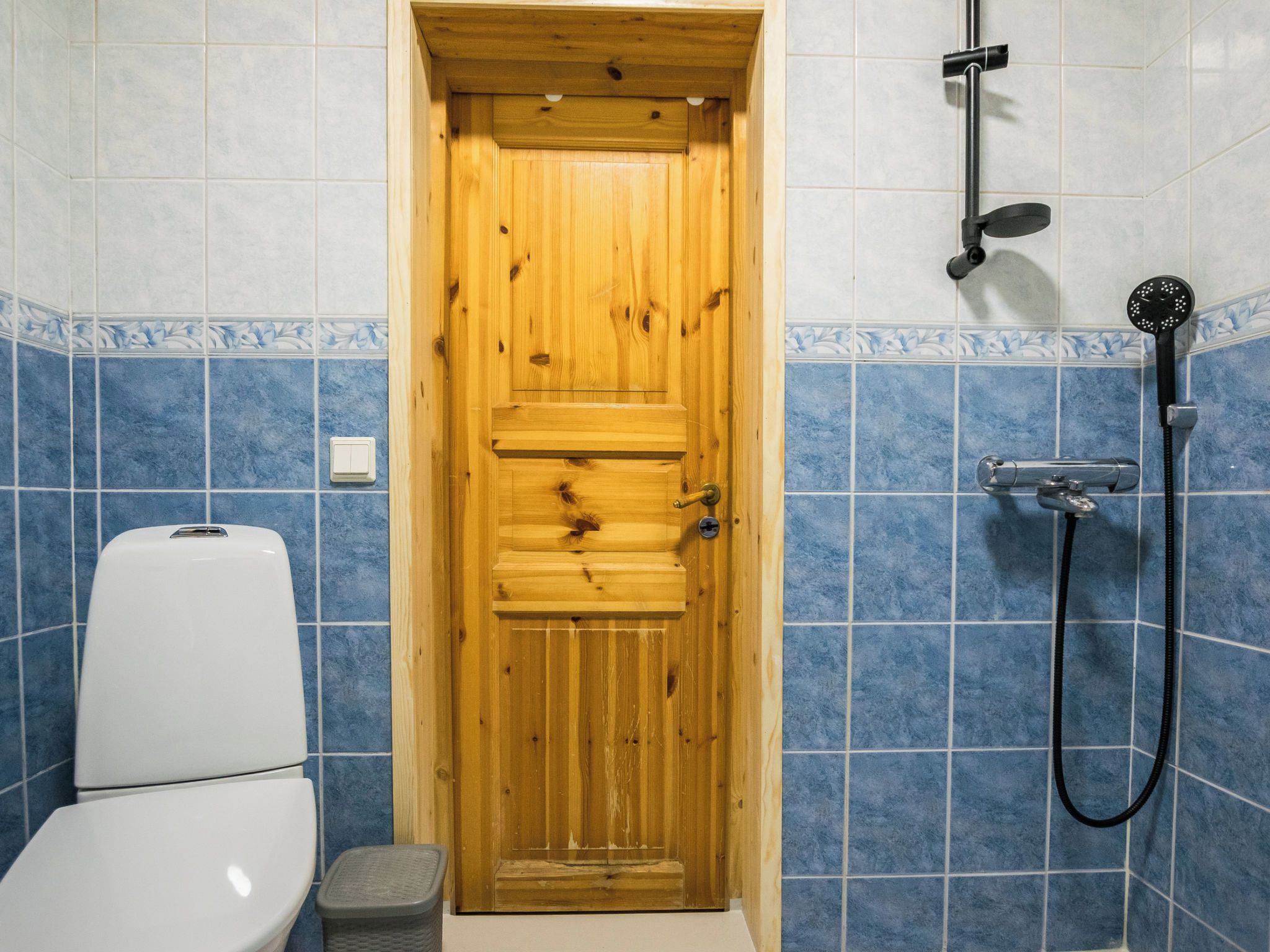 Een houten deur in een badkamer met toilet en douche.