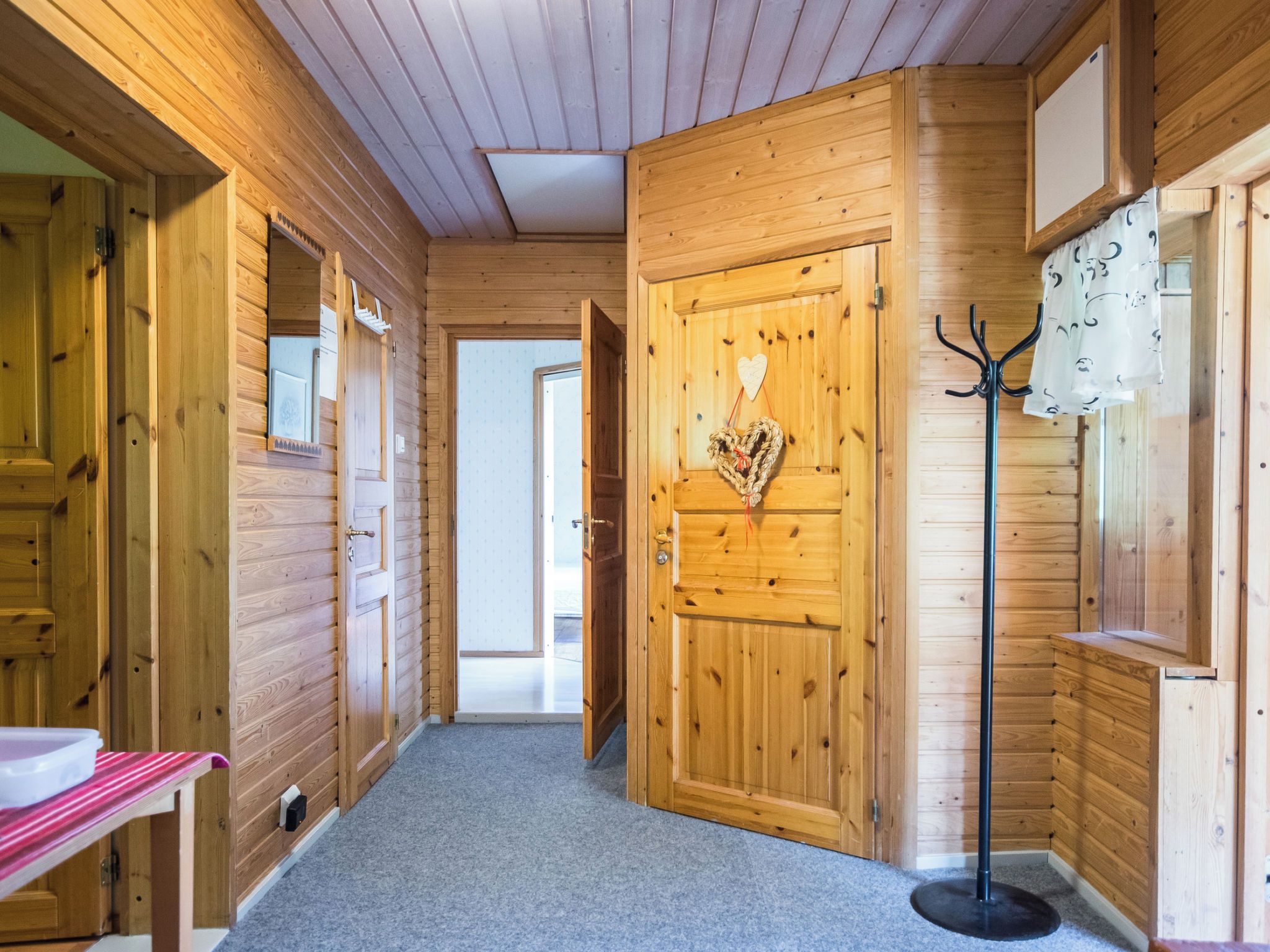 Un interior de madera con un pasillo que lleva a una puerta, un perchero y un banco.