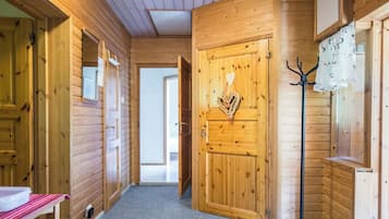 Un interior de madera con un pasillo que lleva a una puerta, un perchero y un banco.