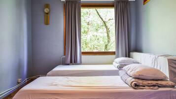 A room with two beds, a window with curtains, a wall clock, and a radiator.