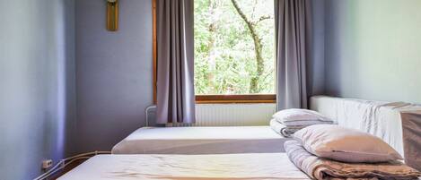 A room with two beds, a window with curtains, a wall clock, and a radiator.