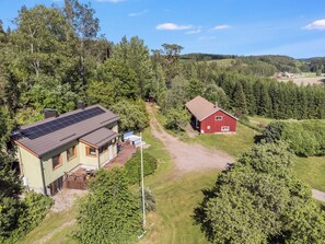 Talo, jossa on aurinkopaneelit, punainen lato ja metsäinen alue.