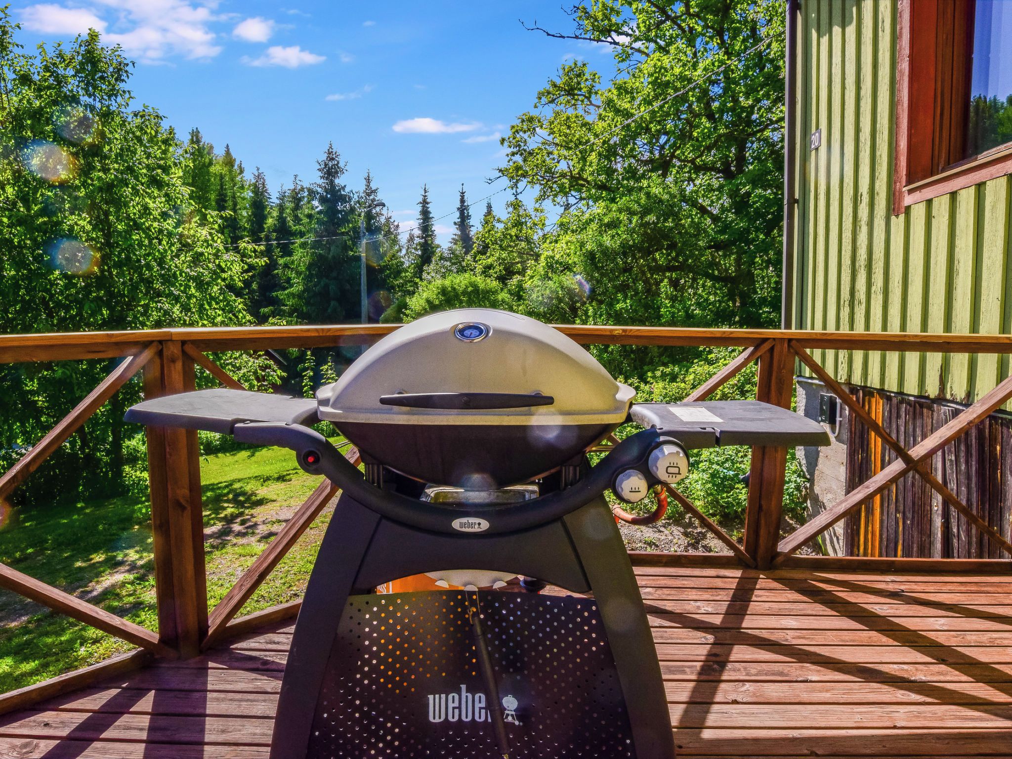 A Weber grill on an outdoor deck with a view of a forested area.