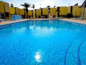 A swimming pool with clear blue water, surrounded by yellow buildings and palm trees.