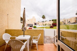 A balcony with a table and chairs, a view of the street, and a building in the background.