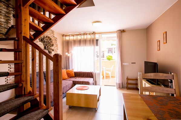A modern living room with a wooden staircase, a sofa, a coffee table, and a TV.