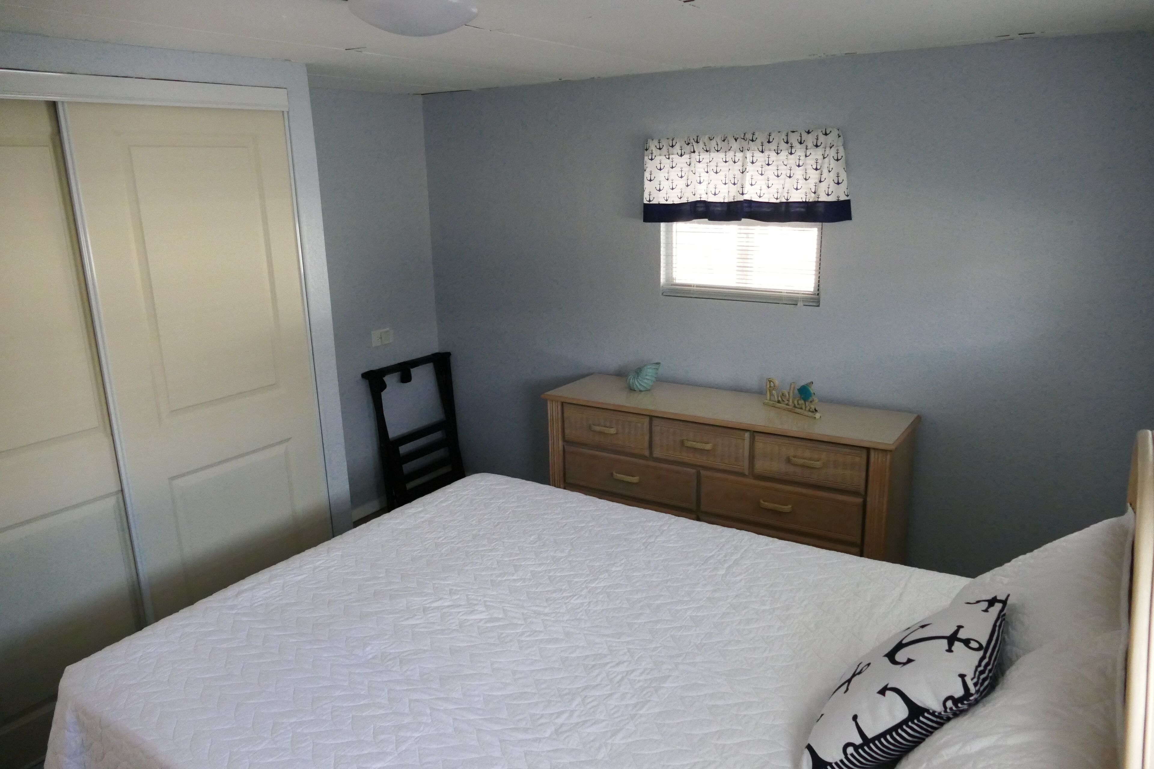 A bedroom with a bed, a dresser, a window with a patterned valance, and a door.