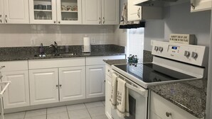A kitchen with white cabinets, a granite countertop, a stove, and a window with blinds. - Beautiful & Spacious Home with Dock Key Largo (Key Largo)