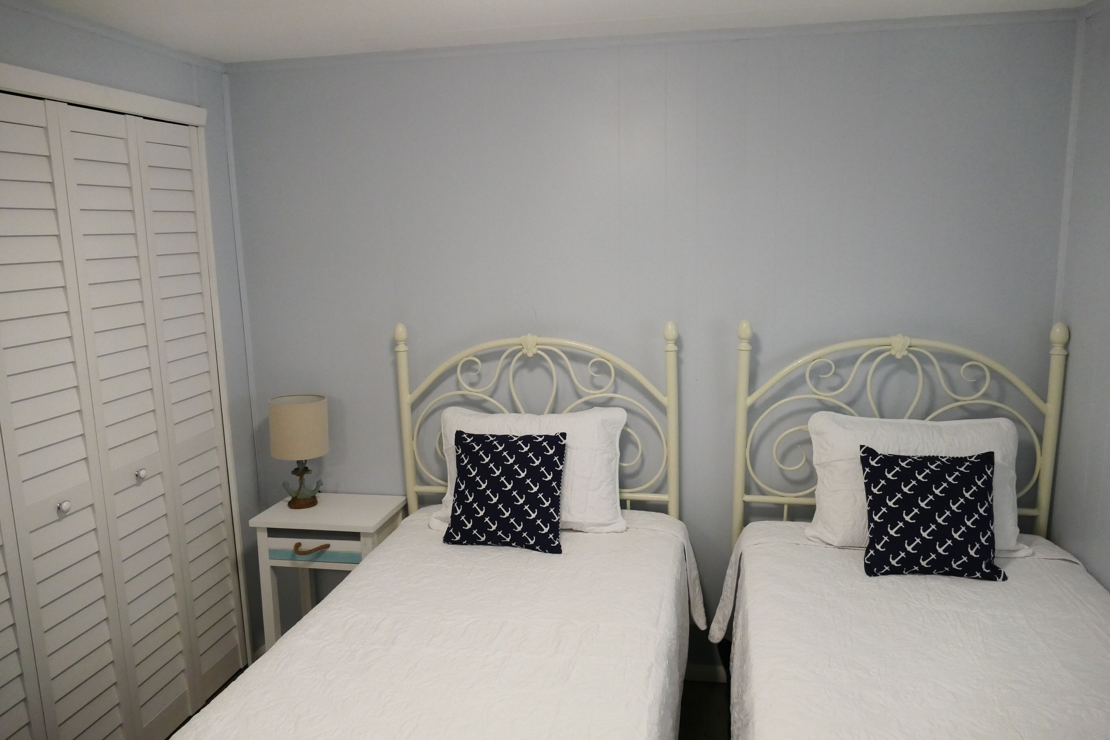 A bedroom with two beds, a nightstand with a lamp, and a white wardrobe.
