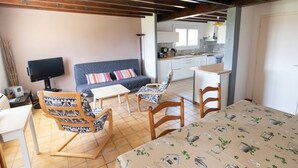 A cozy living room with a sofa, two patterned chairs, a coffee table, and a TV. A kitchen is visible in the background. - Furnished house F3 on one level in Landes Chalosse in a gourmet region. (saint geours d auribat)