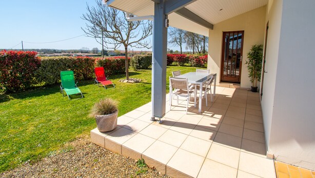 A covered patio with a table and chairs, a green chair, and a red chair outside. - Furnished house F3 on one level in Landes Chalosse in a gourmet region. (saint geours d auribat)
