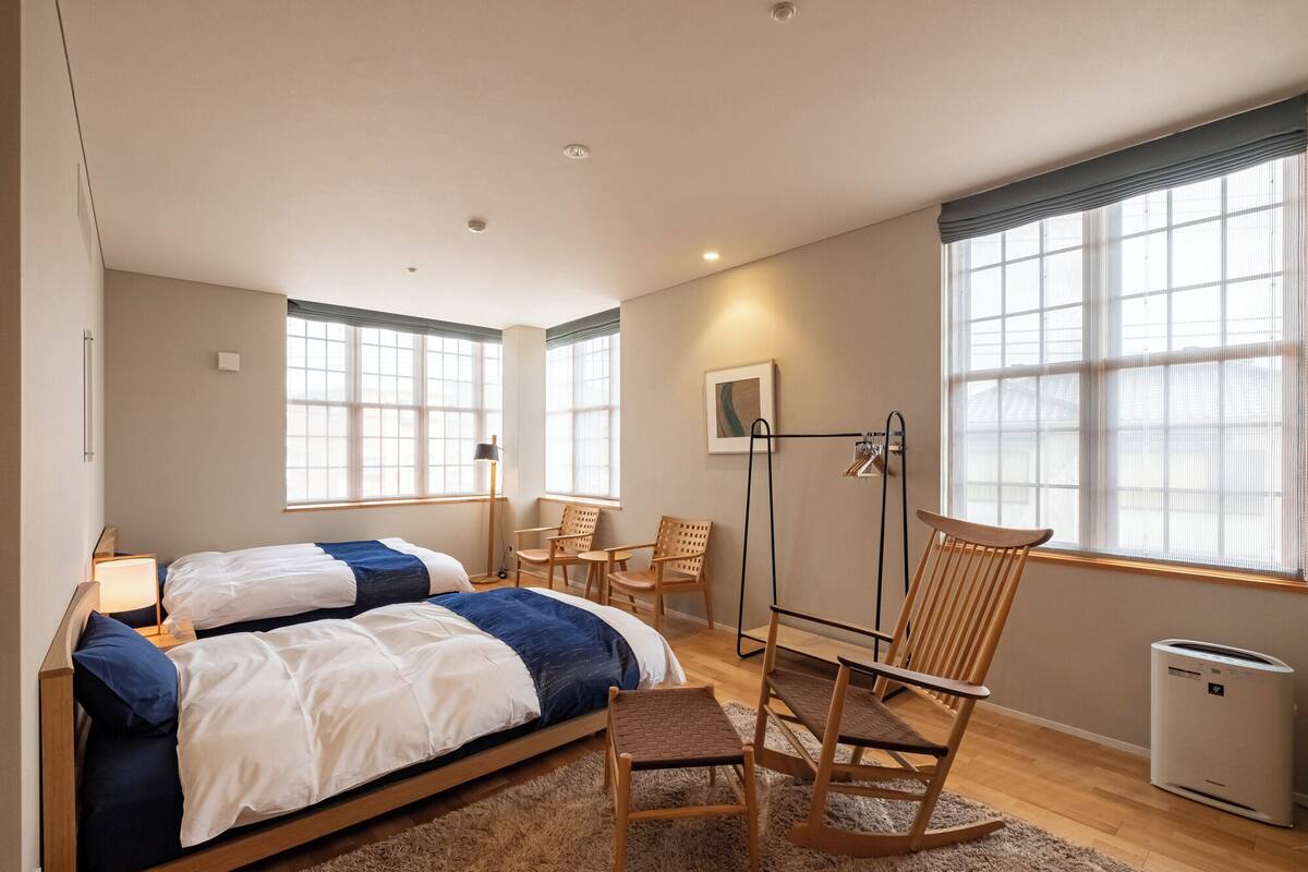A bedroom with two beds, a desk, a chair, and a radiator.