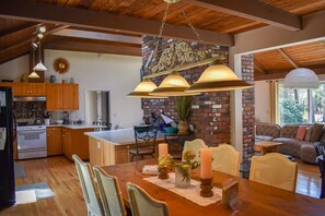 Una cocina amplia con armarios de madera, un comedor con mesa y sillas de madera, y una pared de ladrillo con un sol radiante decorativo.