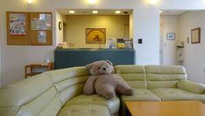 A beige sofa with a teddy bear in a room with a reception desk, a clock, and a framed picture on the wall. - Family Lodge Hatagoya Nasu (Nasu)