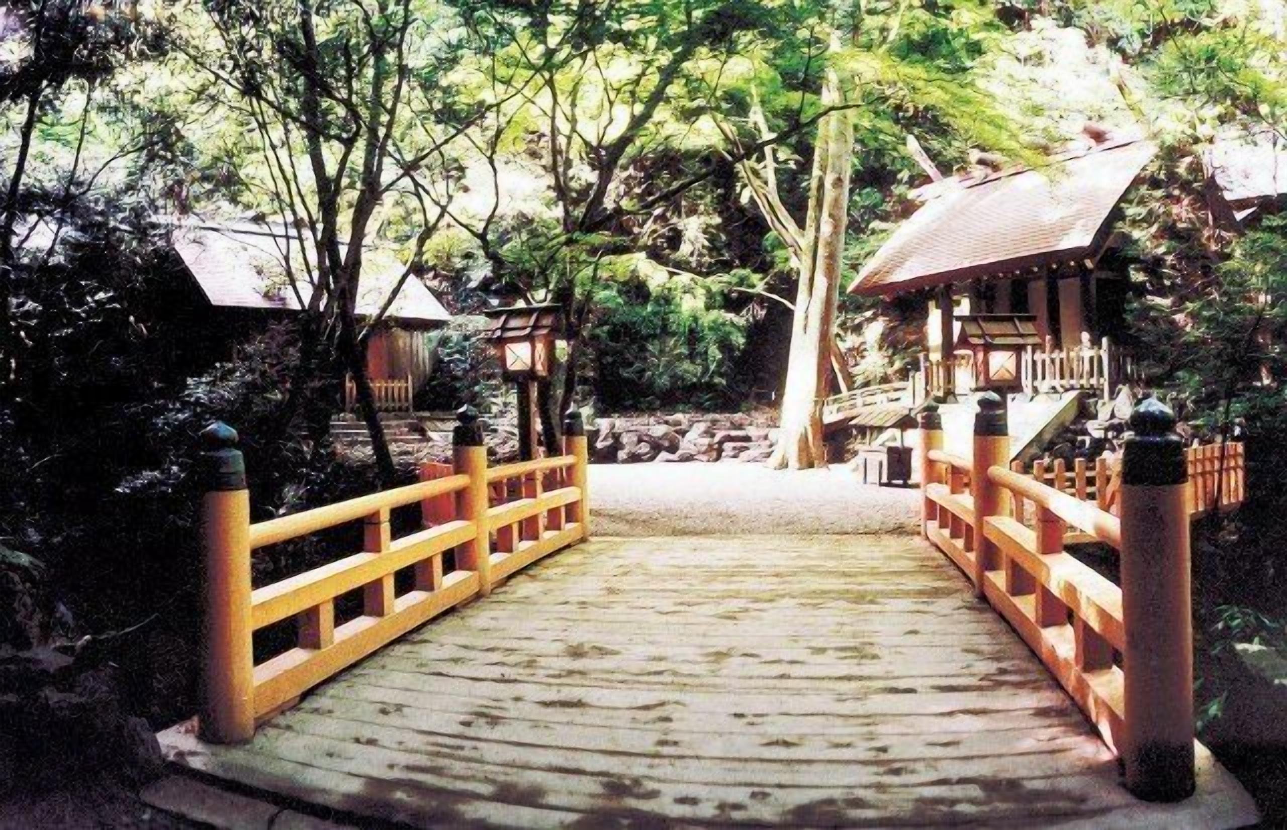A wooden bridge with railings leading to a traditional Japanese structure with a tiled roof.