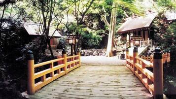 A wooden bridge with railings leading to a traditional Japanese structure with a tiled roof.