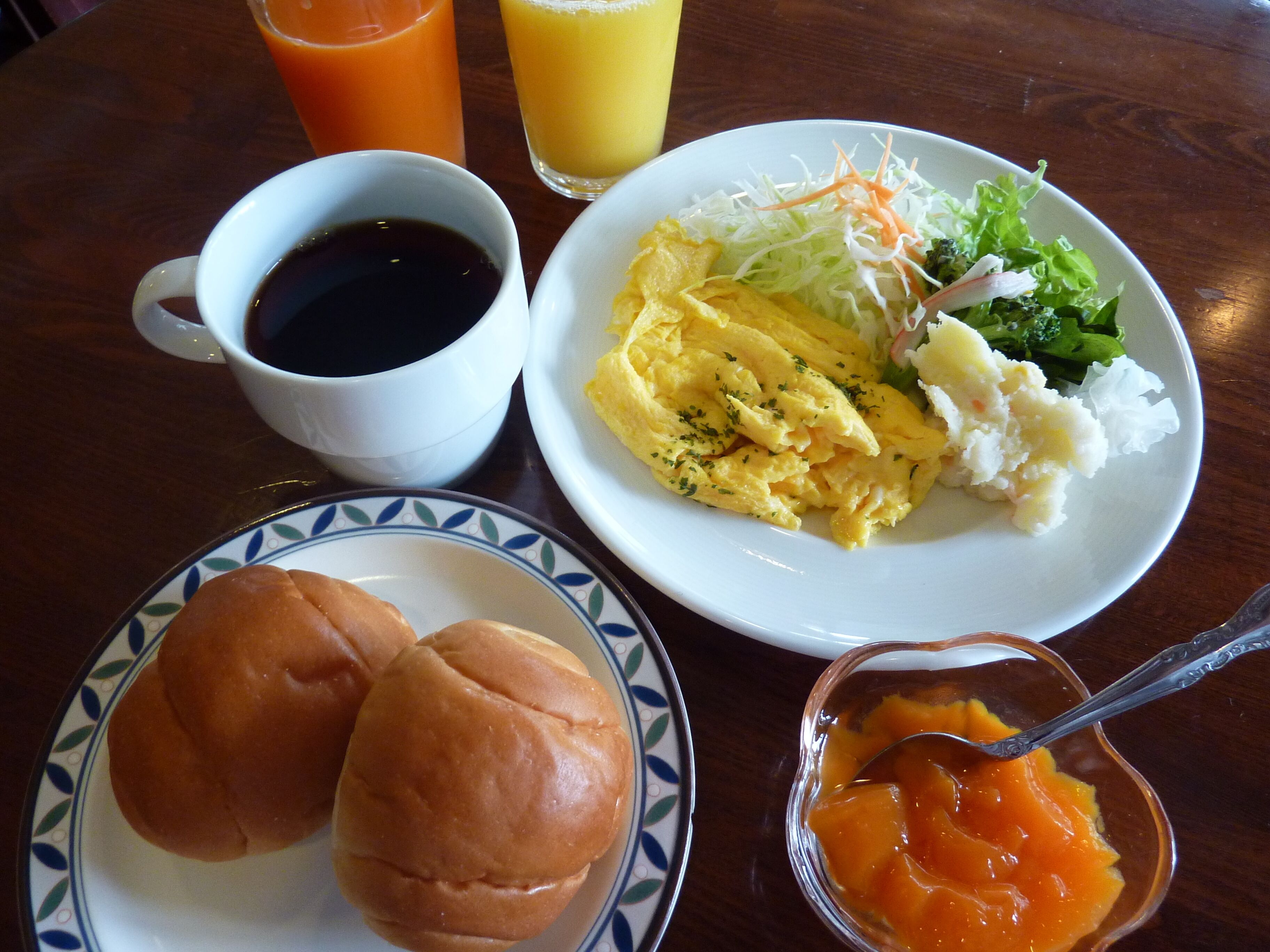 A table with breakfast items including scrambled eggs, toast, a salad, and a bowl of fruit.
