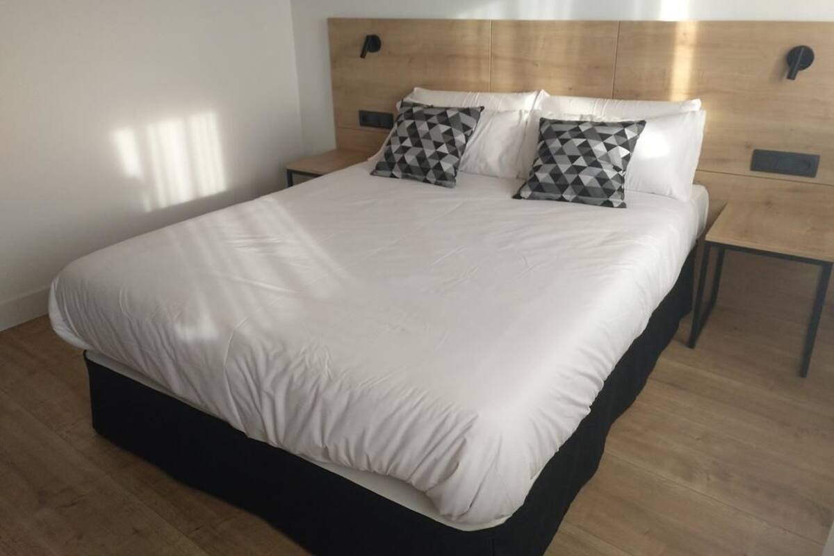 Ein modernes Hotelzimmer mit einem großen Bett, einem Holz-Kopfteil und zwei Nachttischen.