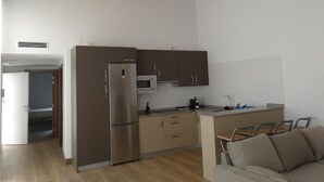 A modern kitchen with a refrigerator, microwave, and wooden cabinets. There is a small dining area with a table and chairs. - Hotel Entrerailes (Casalarreina)