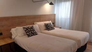 A double bed with a wooden headboard, two bedside tables, and a geometric-patterned pillow. - Hotel Entrerailes (Casalarreina)